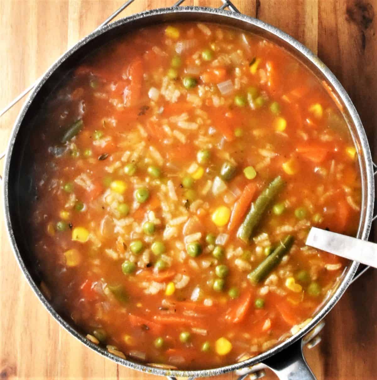 Hearty vegetable and rice soup in pot with spoon.