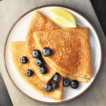 3 folded buckwheat crepes with blueberries and lemon wedge on plate.