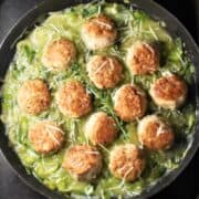 Top down view of chicken meatballs in leek sauce in large pan.