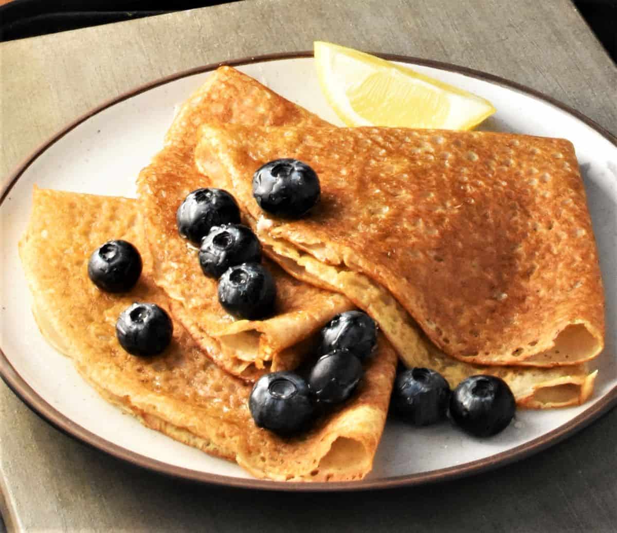 Side view of folded buckwheat flour crepes with blueberries on plate.