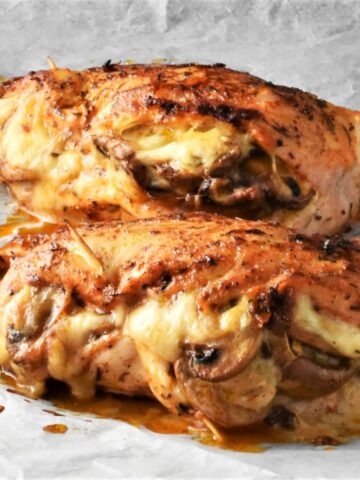 Side view of mushroom and cheese stuffed chicken breasts on parchment.