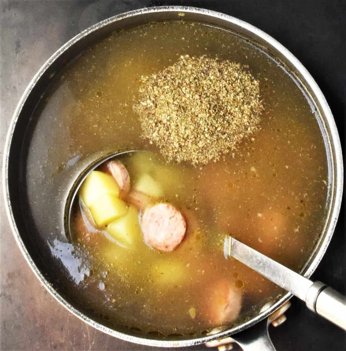 Broth with potatoes. herbs and sausages in pot with ladle.