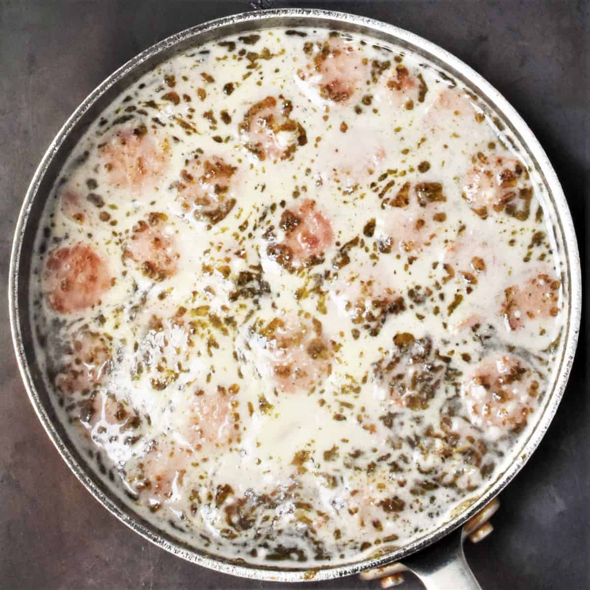 Large pot with white coloured soup and pieces of sausage floating on top.