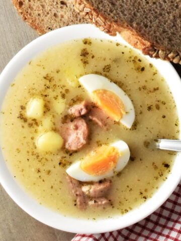 Top down view of zurek soup with sausage and eggs in white bowl with spoon.