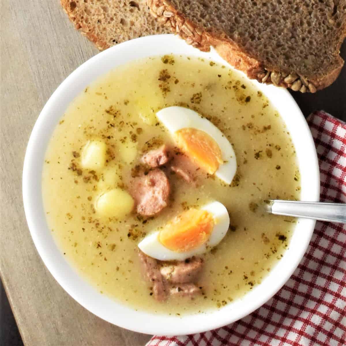 Top down view of zurek soup with sausage and eggs in white bowl with spoon.