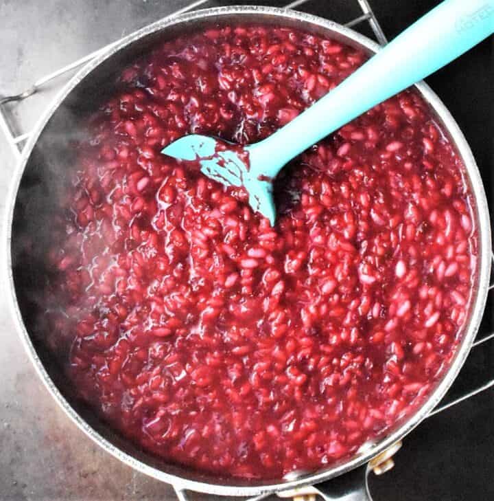 Beet coloured risotto mixture in large pot with blue silicon spoon.