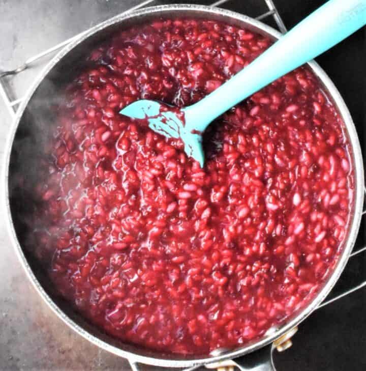 Top down view of creamy beet risotto in pot with blue spoon.