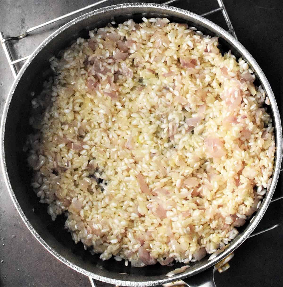 Risotto rice with chopped shallots in pot.