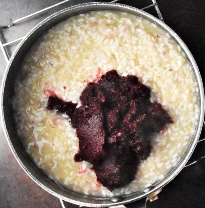 Creamy risotto with beet puree in large black pot.