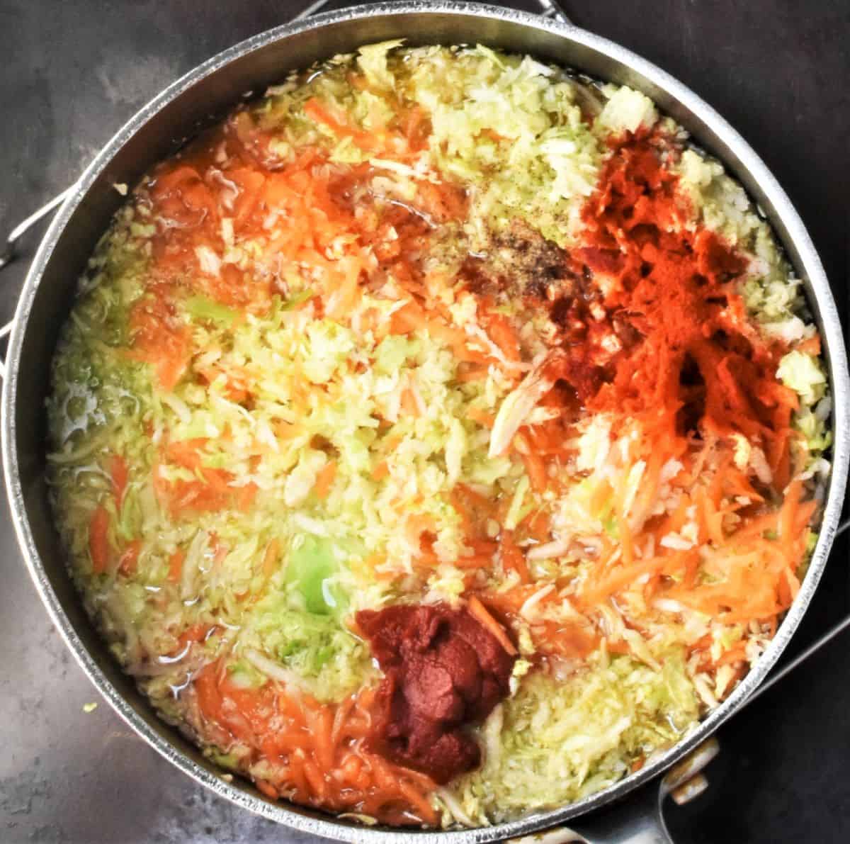 Shredded cabbage, carrot and spices in large pot.
