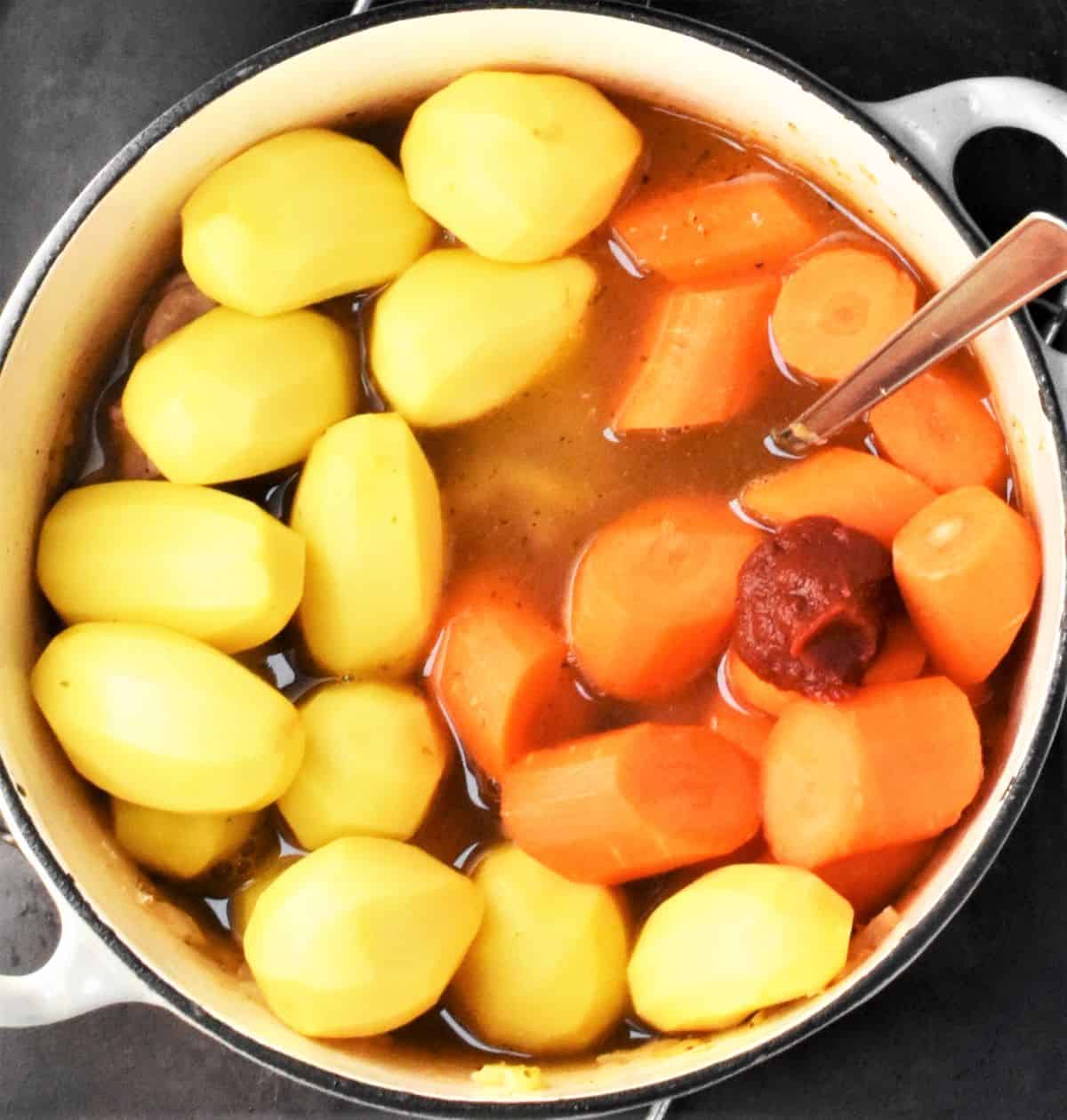 Potatoes, carrots and stock in large pot with spoon.