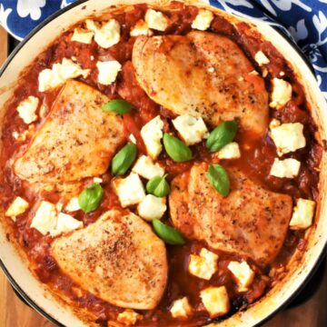 Top down view of 4 chicken breasts in tomato sauce with feta in round dish.