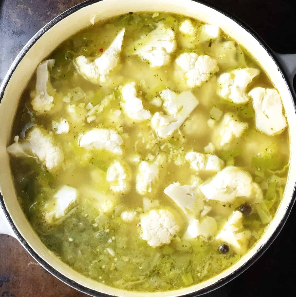 Top down view of chunks of cauliflower in soup in white pot.
