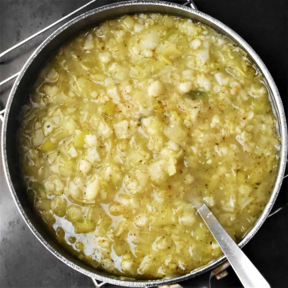 Chunky soup with cauliflower and leek in large pot with spoon.