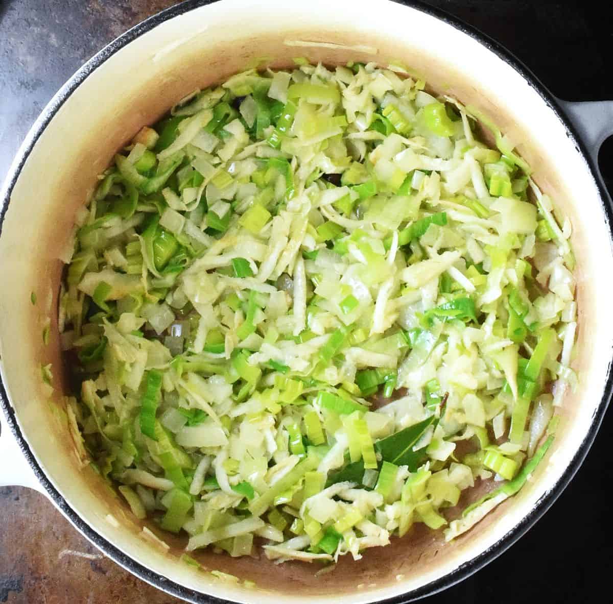 Top down view of finely chopped vegetables in bottom of large white pot.