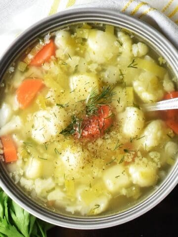 Top down view of Polish cauliflower soup in grey bowl with spoon.