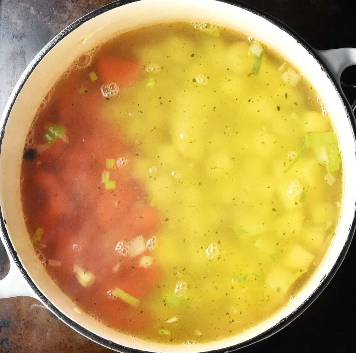 Cubed vegetables with stock in large white pot.