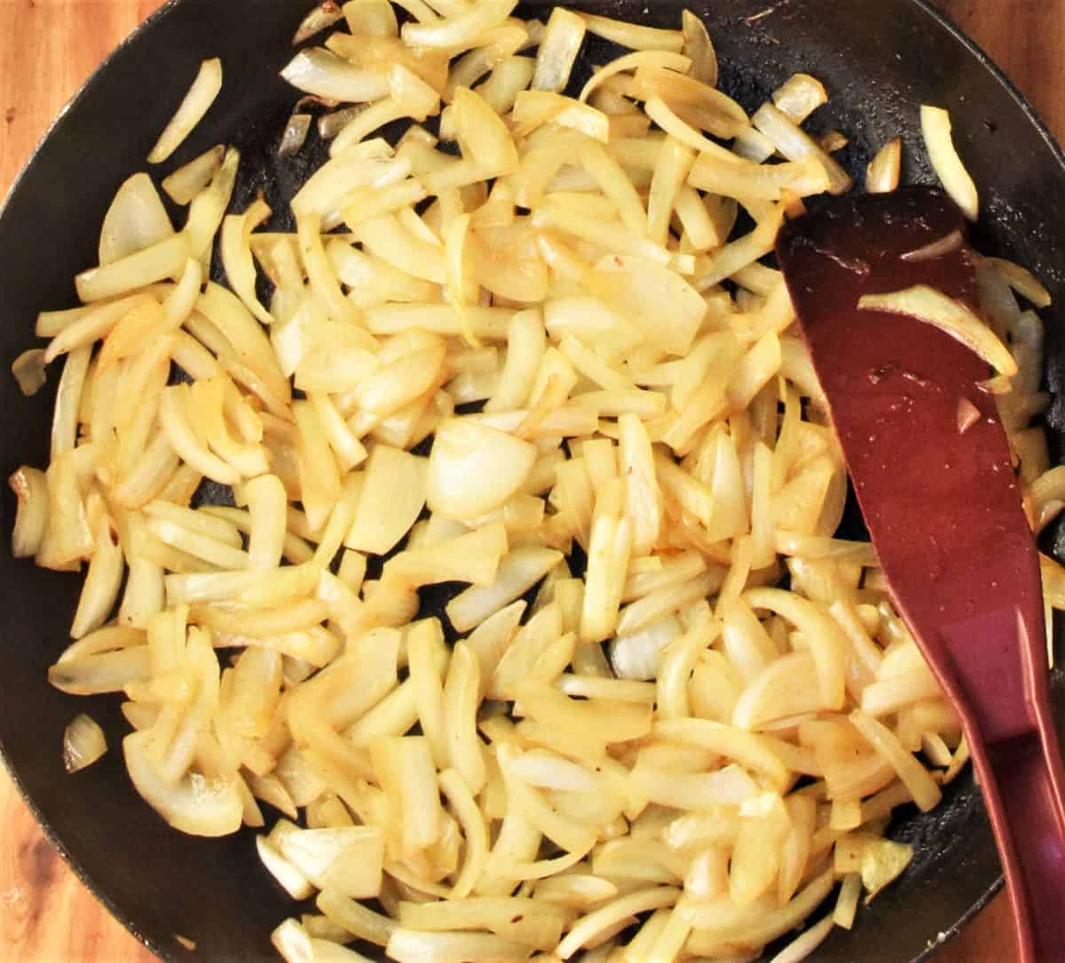 Browning sliced onion in pan with red spatula.
