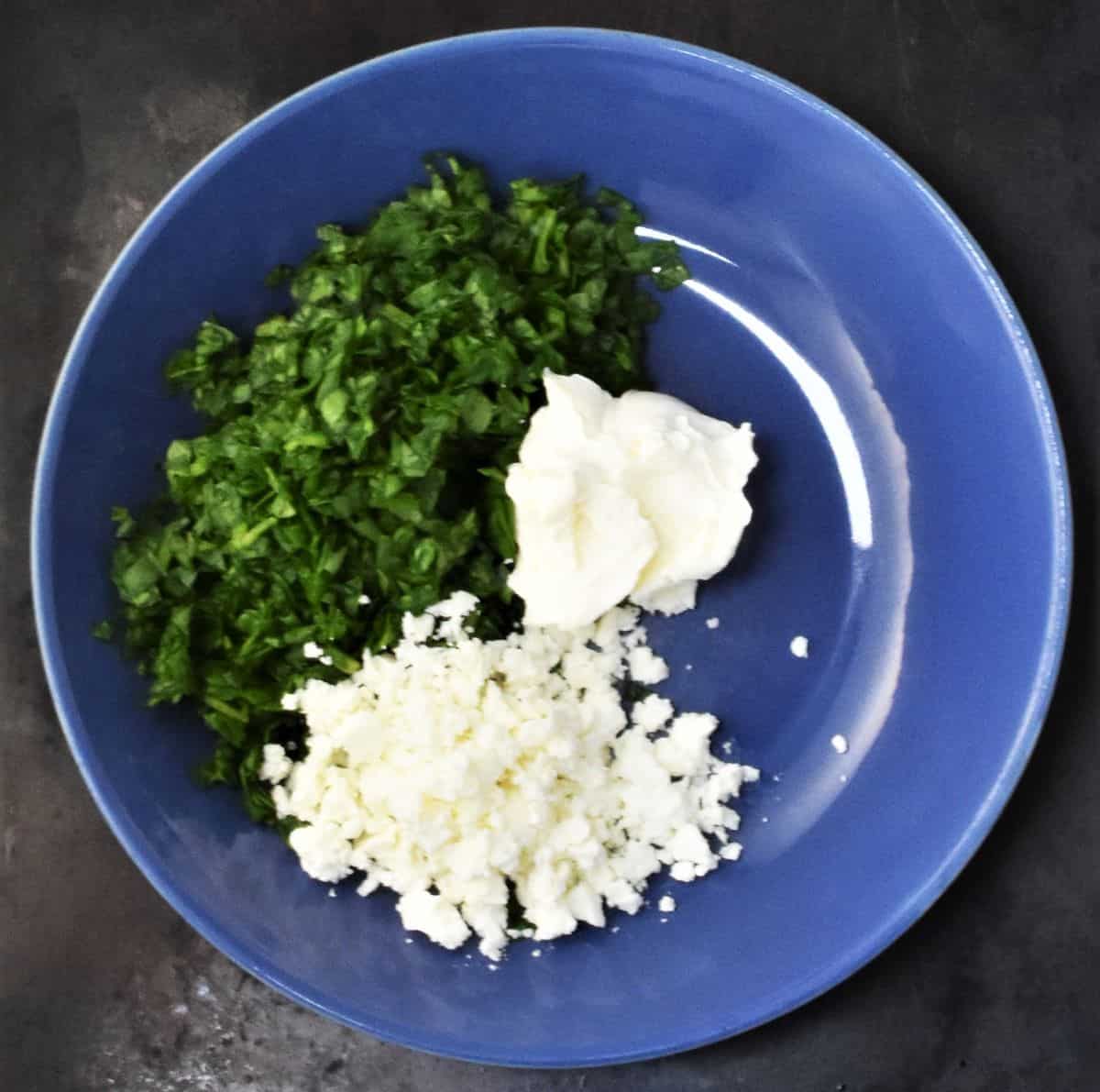 Chopped spinach, crumbled feta and cream cheese in blue bowl.