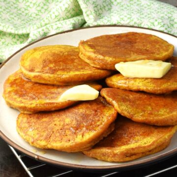 Side view of healthy pumpkin pancakes with butter on white plate.