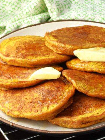 Side view of healthy pumpkin pancakes with butter on white plate.