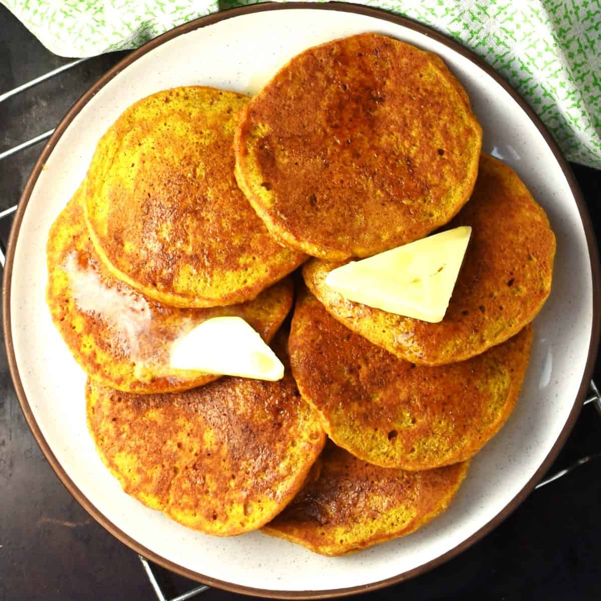 Top down view of lightly browned healthy pumpkin pancakes with knobs of butter and syrup on plate.