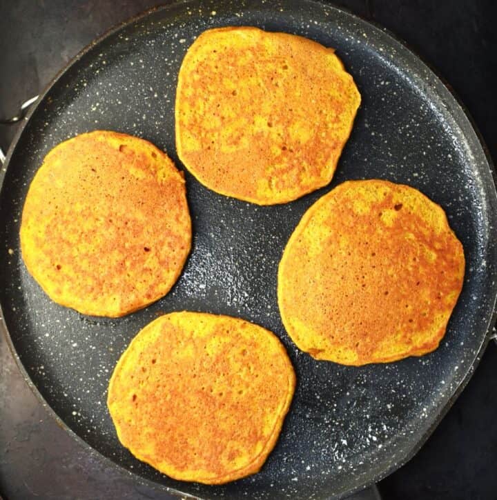 4 lightly browned healthy pumpkin pancakes on top of flat pan.