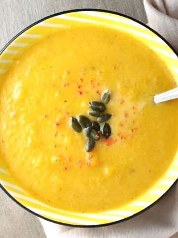 Top down view of creamy Polish pumpkin soup in yellow bowl with spoon.