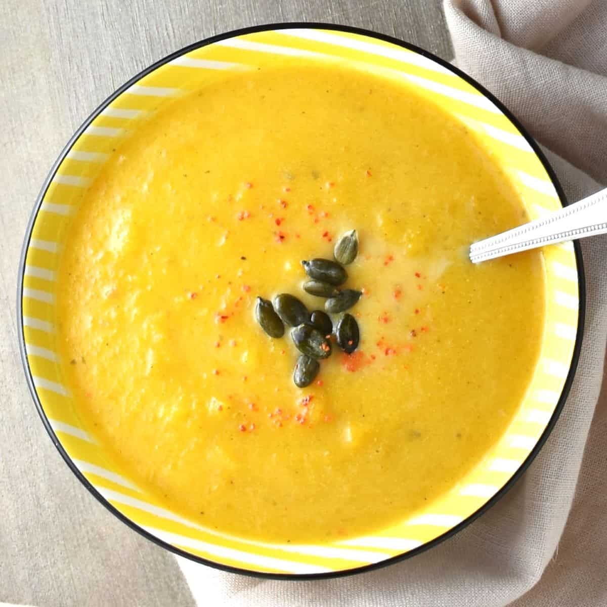 Top down view of creamy Polish pumpkin soup in yellow bowl with spoon.