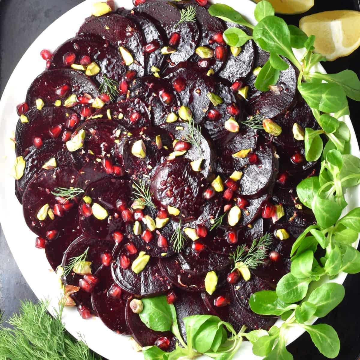Top down view of beet carpaccio with pomegranate seeds on white plate.