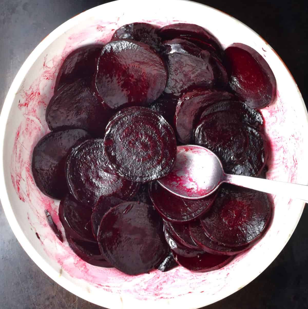 Top down view of sliced beets in white bowl with spoon.