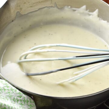 Close-up side view of sour cream sauce in pot with whisk.