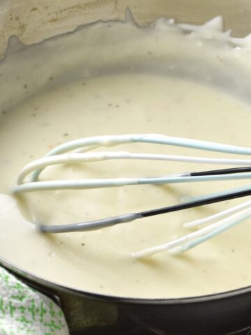 Close-up side view of sour cream sauce in pot with whisk.