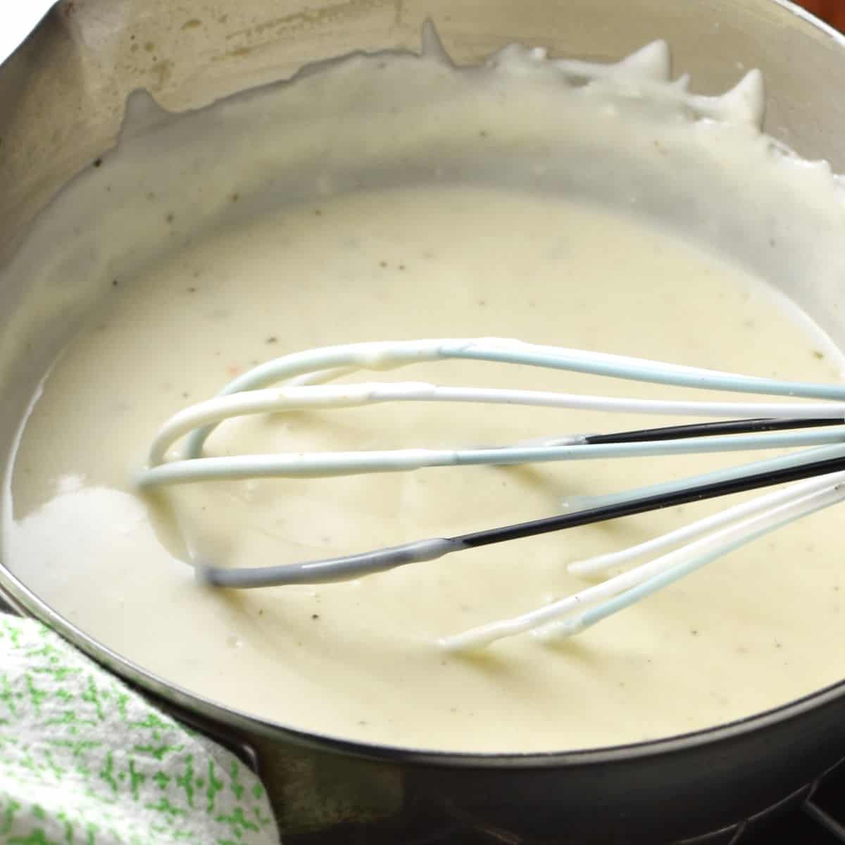 Close-up side view of sour cream sauce in pot with whisk.