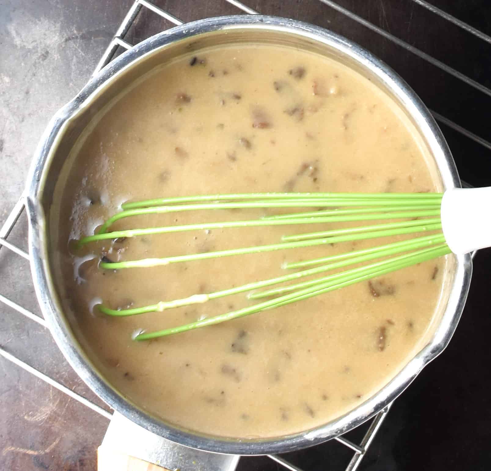 Creamy sauce with finely chopped wild mushrooms  in pan with whisk.