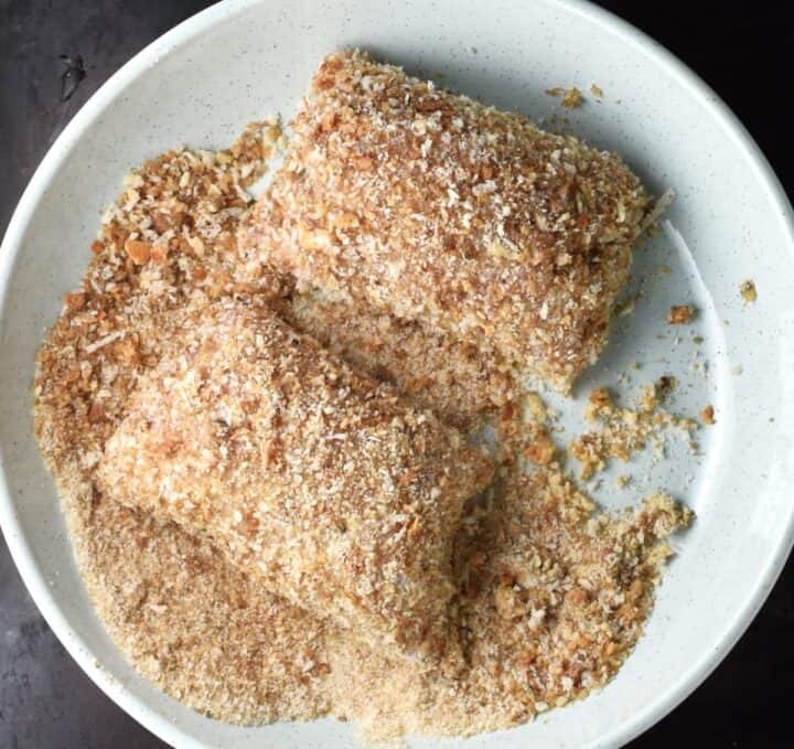 2 chicken-roll-ups coated in breadcrumbs in shallow bowl.