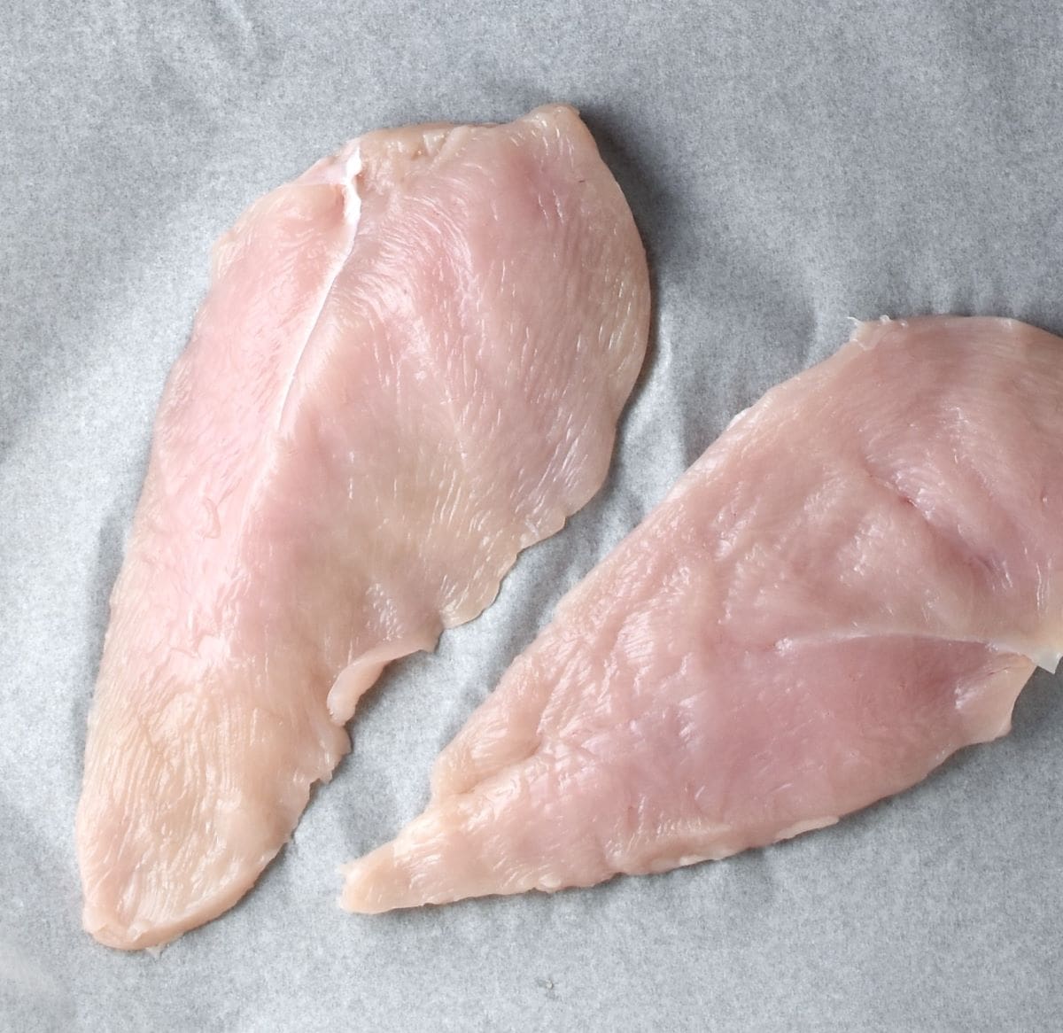 Top down view of 2 chicken breast halves on paper.