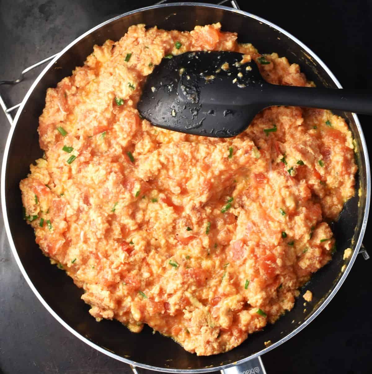 Top down view of tomato scrambled eggs with black spatula in pan.