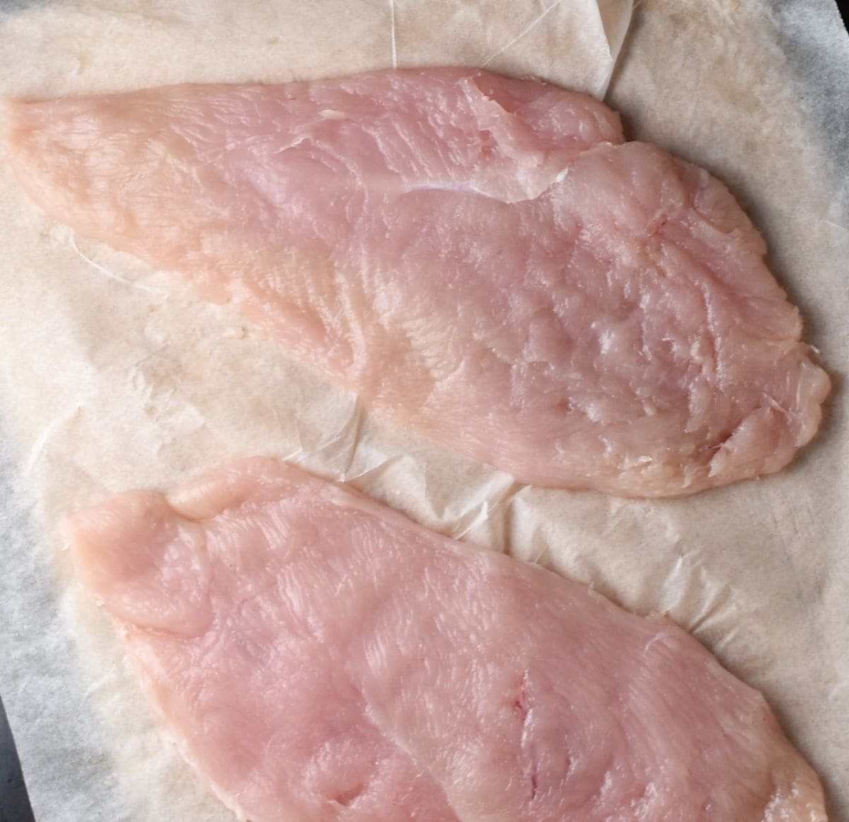2 flattened pieces of chicken breast on parchment.