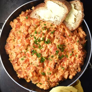 Top down view of scrambled eggs with tomatoes and bread in pan.