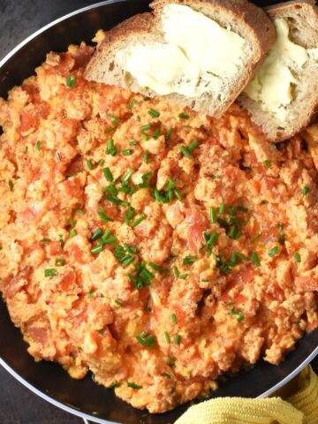 Top down view of scrambled eggs with tomatoes and bread in pan.