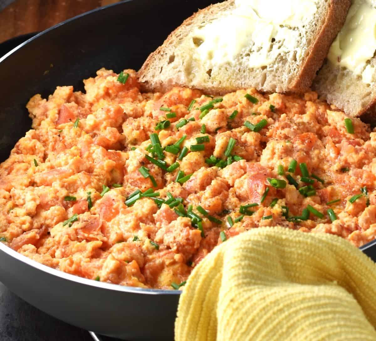 Side view of scrambled eggs and tomato with bread in pan.