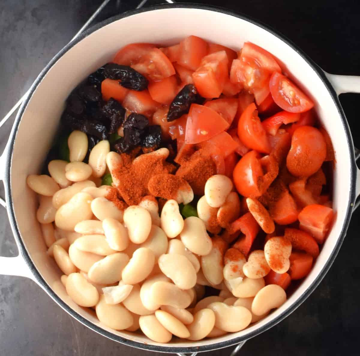 Chopped vegetables and white beans for goulash in pot.