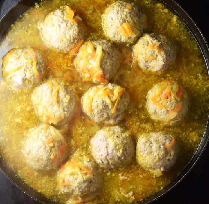 Cooking meatballs in broth in shallow pan.