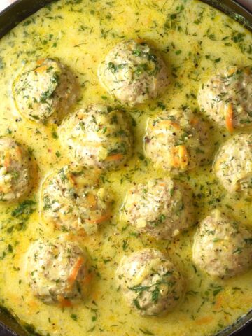 Top down view of Polish meatballs in dill sauce in shallow pan.