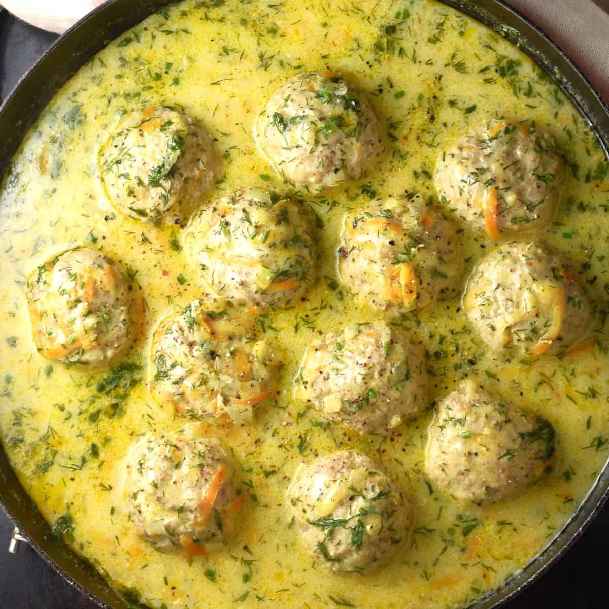 Top down view of Polish meatballs in dill sauce in shallow pan.