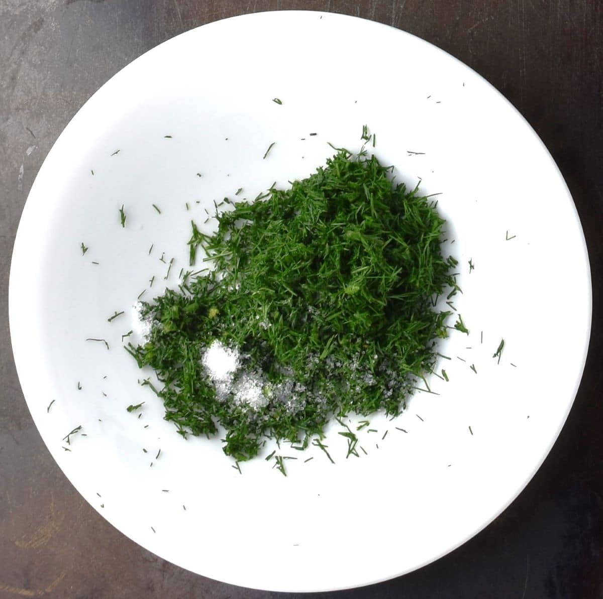 Chopped dill with salt in white bowl.