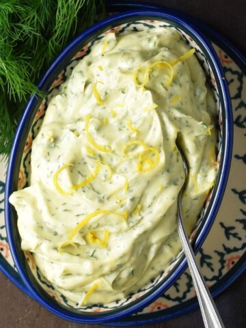 Dill mayonnaise in oval blue bowl with spoon and fresh dill in top left corner.