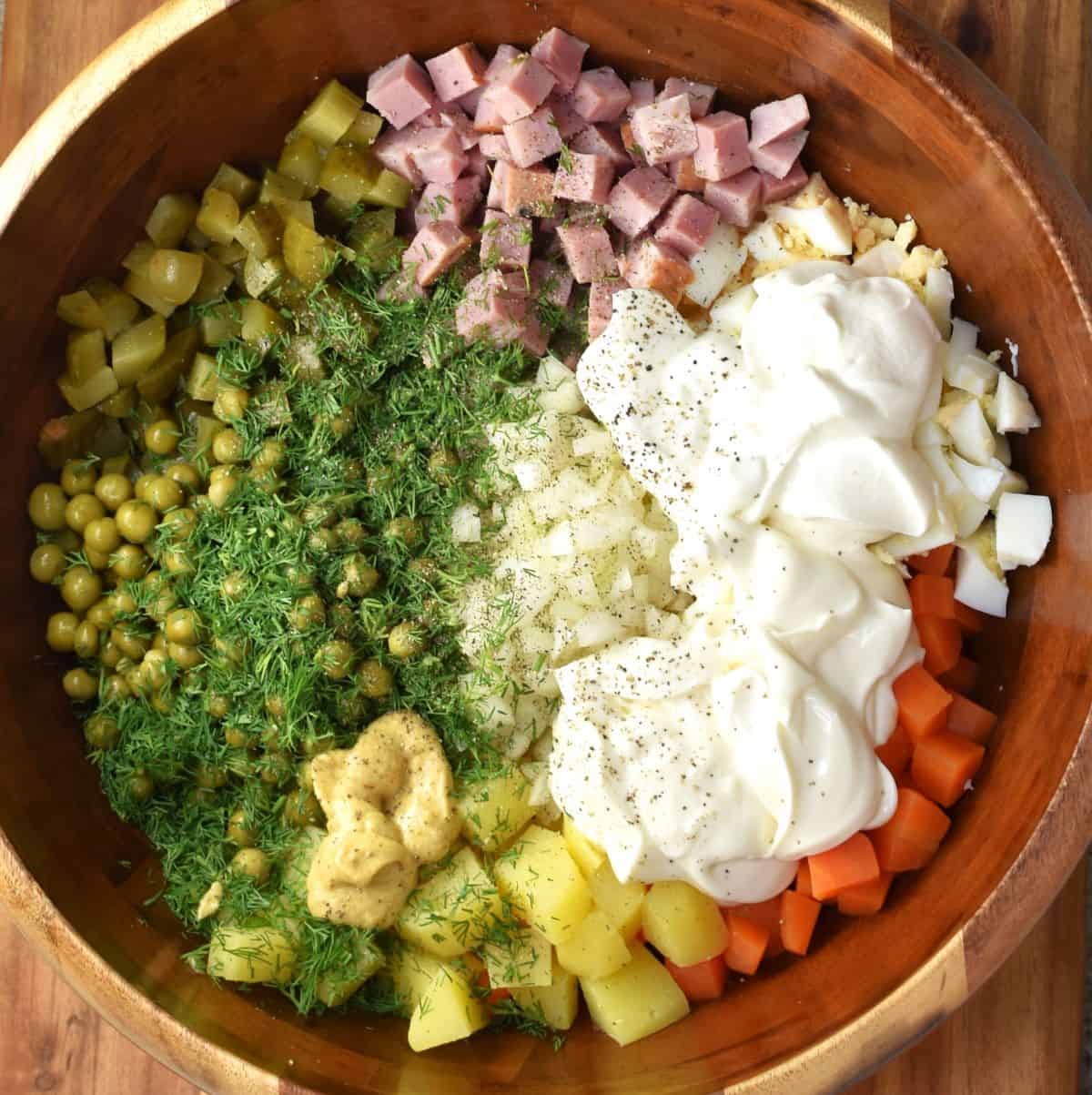 Top down view of vegetables, dill and mayonnaise for Russian potato salad in wooden bowl.
