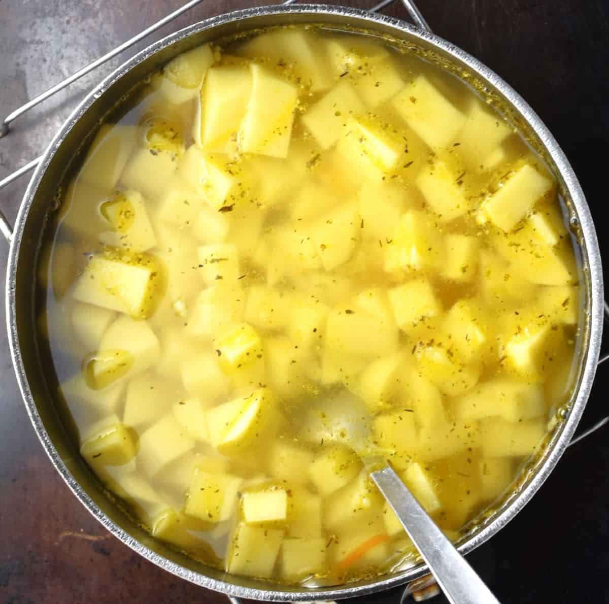 Top down view of cubed potatoes in soup pot with spoon.